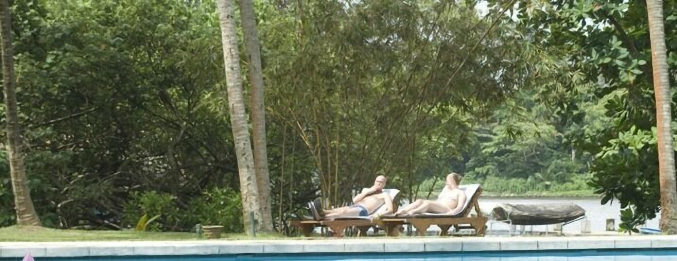A poolside area with lounge chairs and a view of a body of water surrounded by trees.
