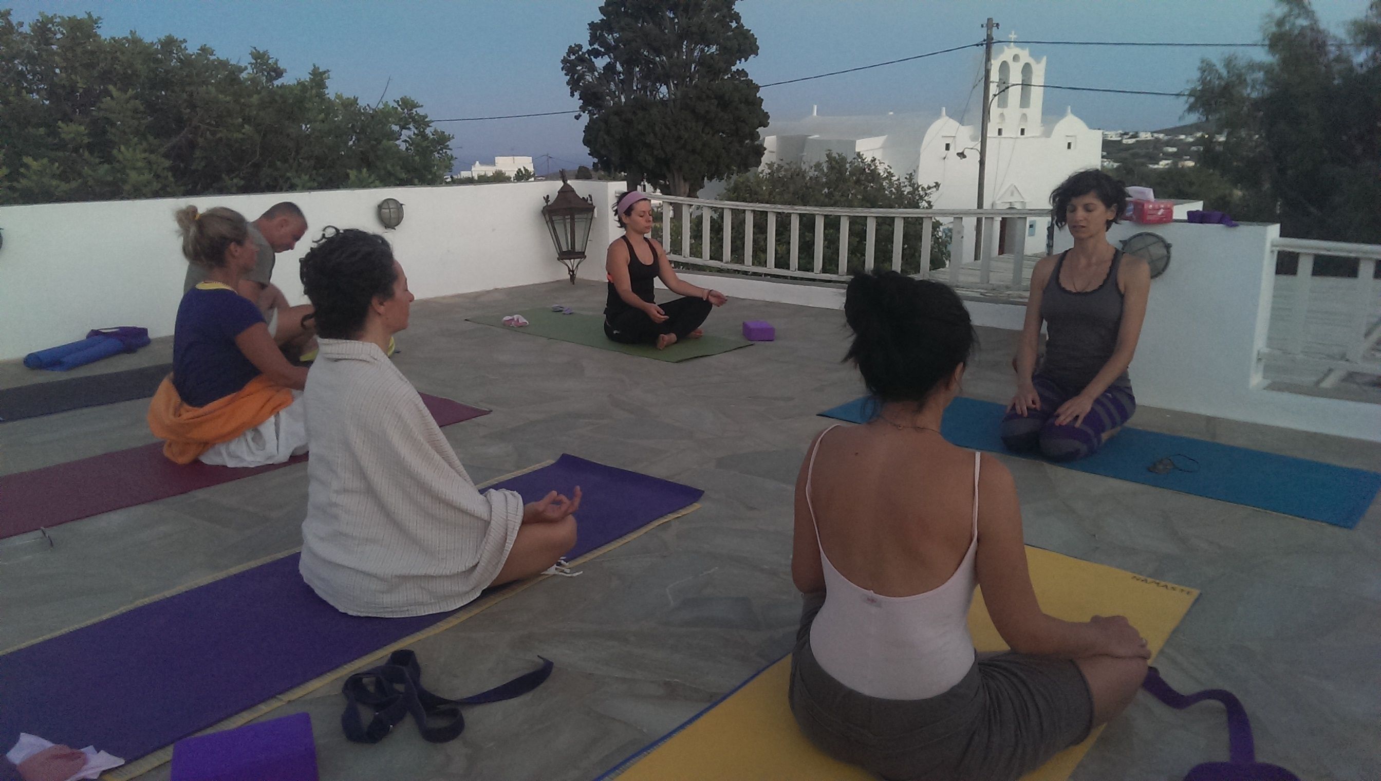 A group of people on yoga mats on a rooftop with a church in the background.
