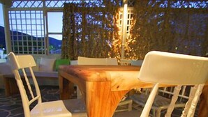 An outdoor dining area with a wooden table and white chairs, set on a patterned stone floor.