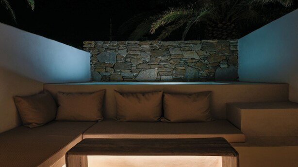 A modern outdoor seating area with a stone wall backdrop, a cushioned bench, and a wooden table.