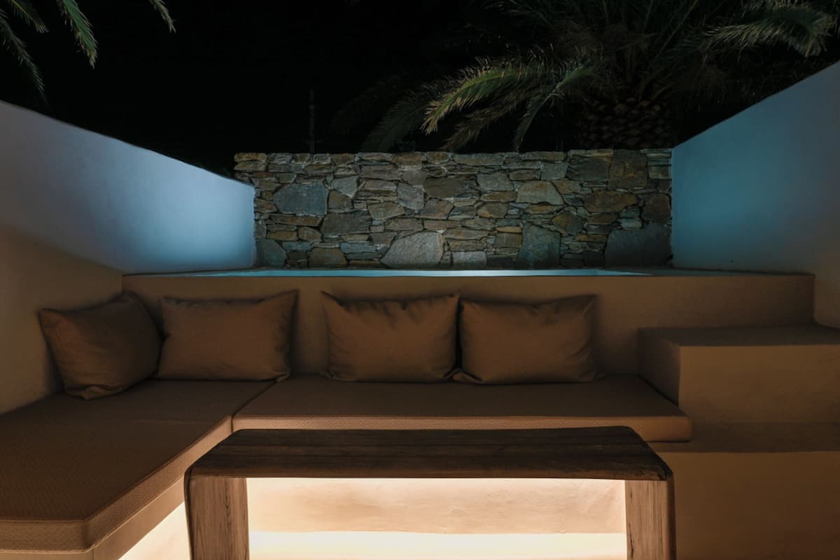 A modern outdoor seating area with a stone wall backdrop, a cushioned bench, and a wooden table.