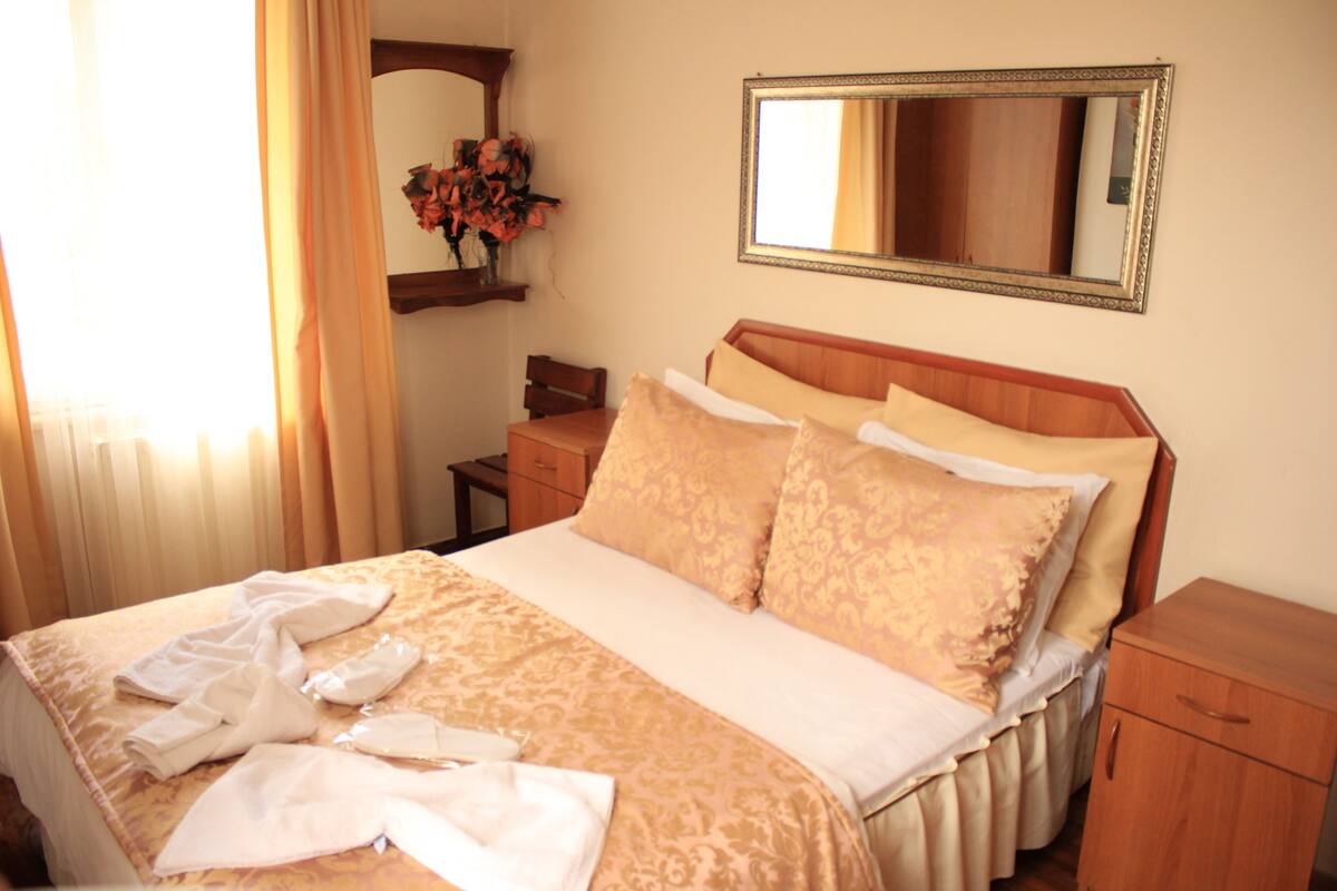 A hotel room with a bed, a nightstand, a dresser, a mirror, and a window with curtains.