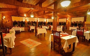 A restaurant with wooden interiors, multiple tables, and hanging light fixtures. - El Rio Motel (Sile)