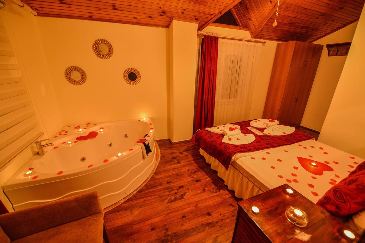 A bedroom with a large bathtub, a bed with rose petals, and a wooden ceiling.