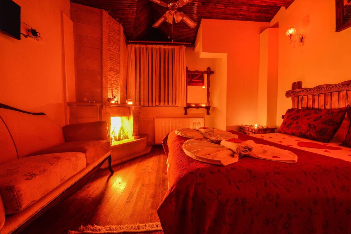 A cozy room with a bed, a chair, a small table with a lamp, and a ceiling fan.