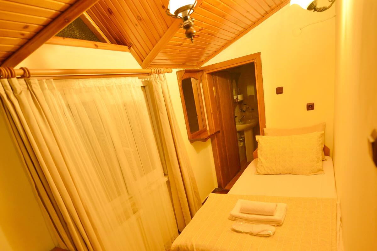 A small, cozy bedroom with a single bed, a nightstand, and a wooden ceiling.