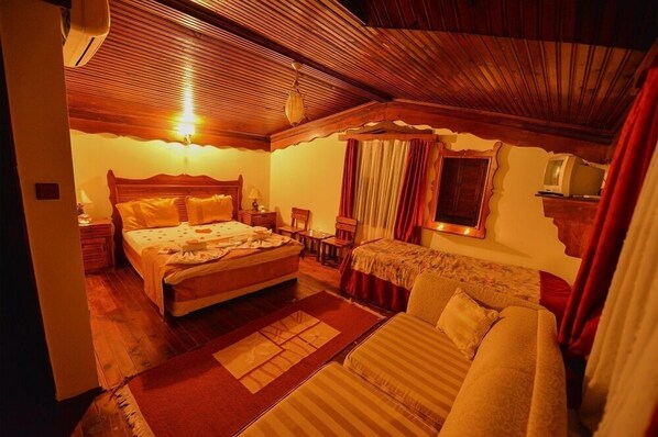 A cozy bedroom with a wooden ceiling, a large bed, a sofa, and a television on a shelf.