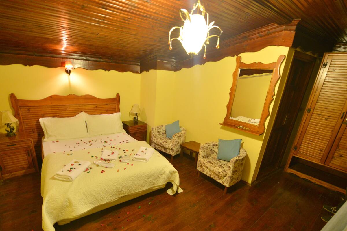 A bedroom with a wooden bed, two nightstands, a chair, a mirror, and a wooden ceiling.