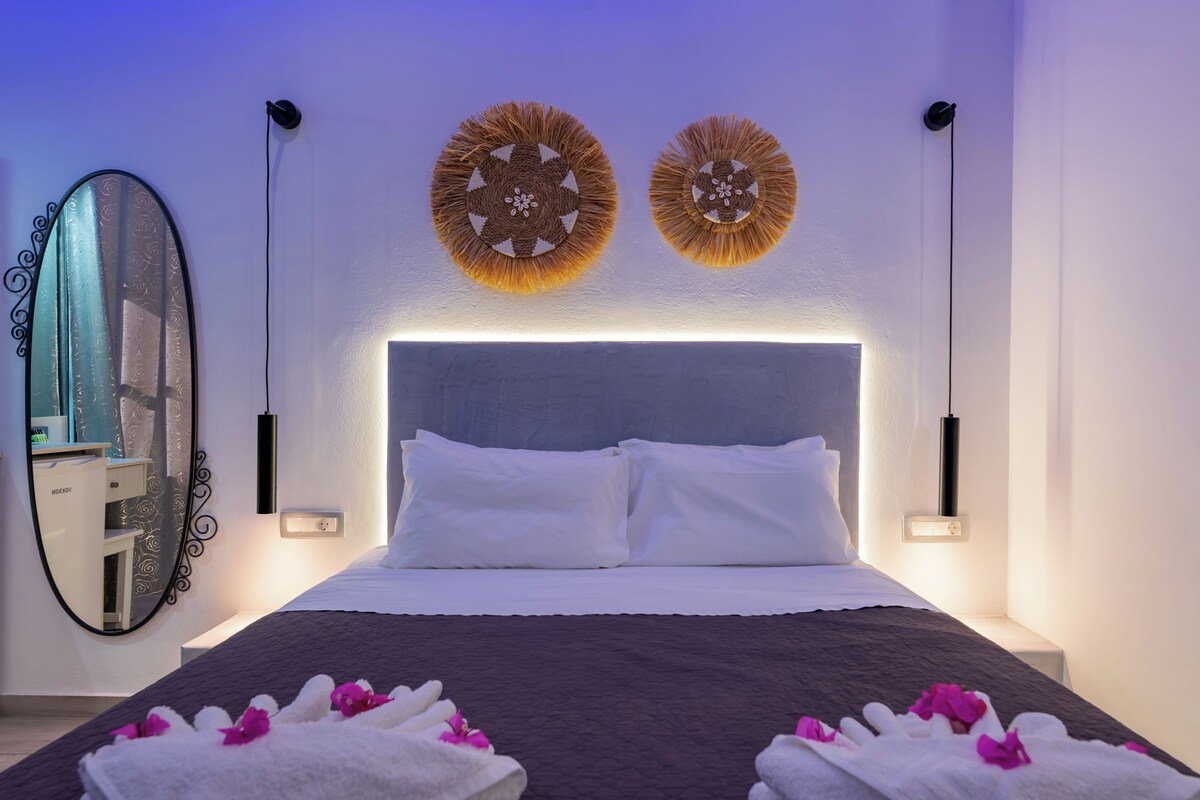 A modern bedroom with a large bed, two wall-mounted lamps, a mirror, and a decorative wall piece.