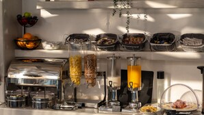A breakfast buffet with various food options, including cereal, orange juice, and meat dishes. - Villa Anemomilos (Santorini)