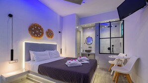 A modern bedroom with a large bed, bedside tables, a desk with chairs, and a TV mounted on the wall. - Villa Anemomilos (Santorini)