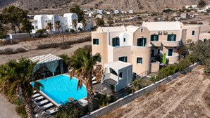 A modern resort with a swimming pool, palm trees, and Mediterranean-style architecture. - Villa Anemomilos (Santorini)