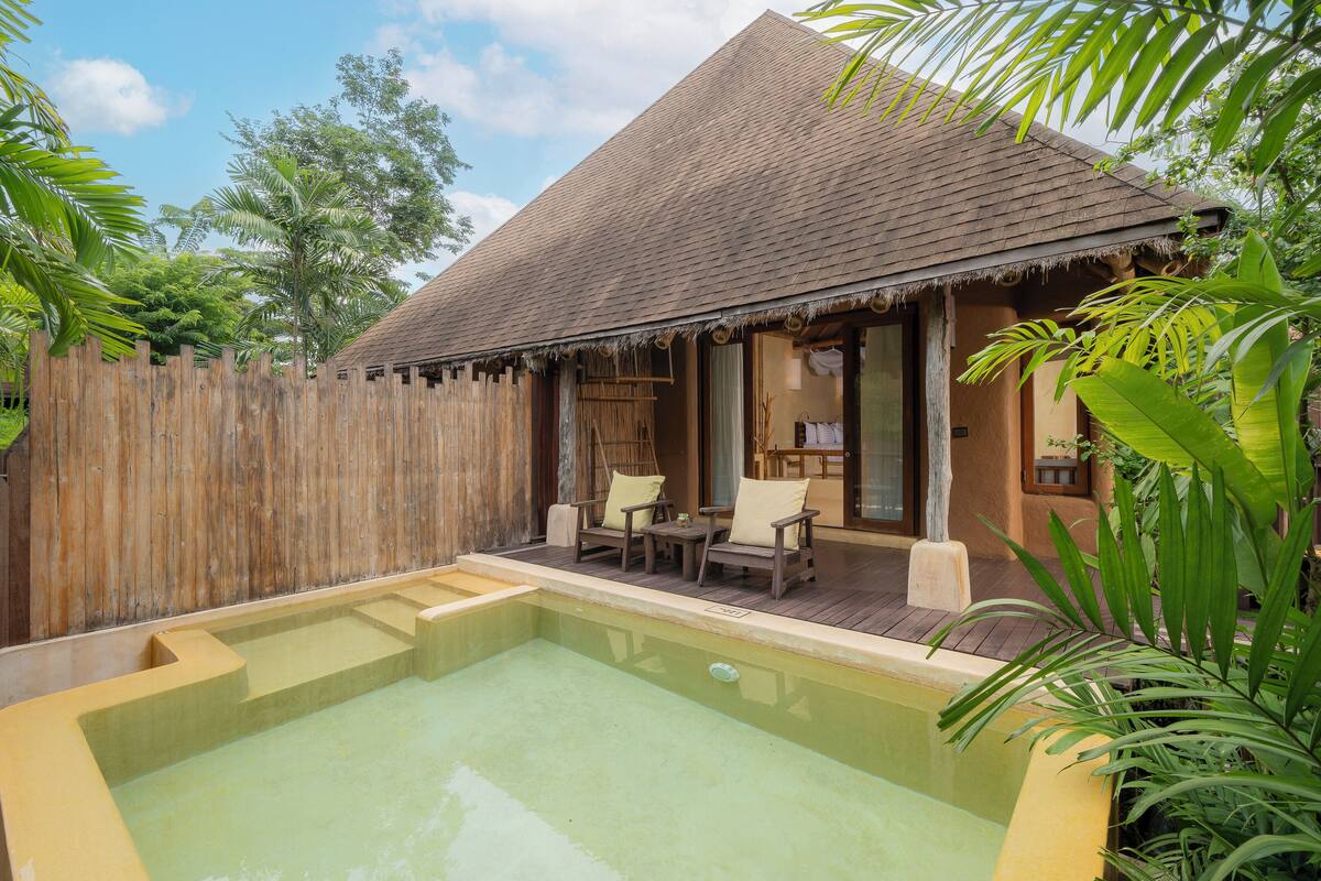 A poolside area with a wooden deck, a thatched-roof structure, and a wooden fence.