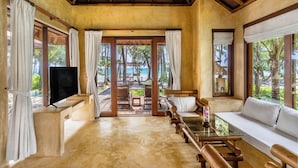A room with a wooden ceiling, large windows with white curtains, a sofa, a TV, and a view of the beach. - High Season Pool Villa & Spa (Ko Kood)
