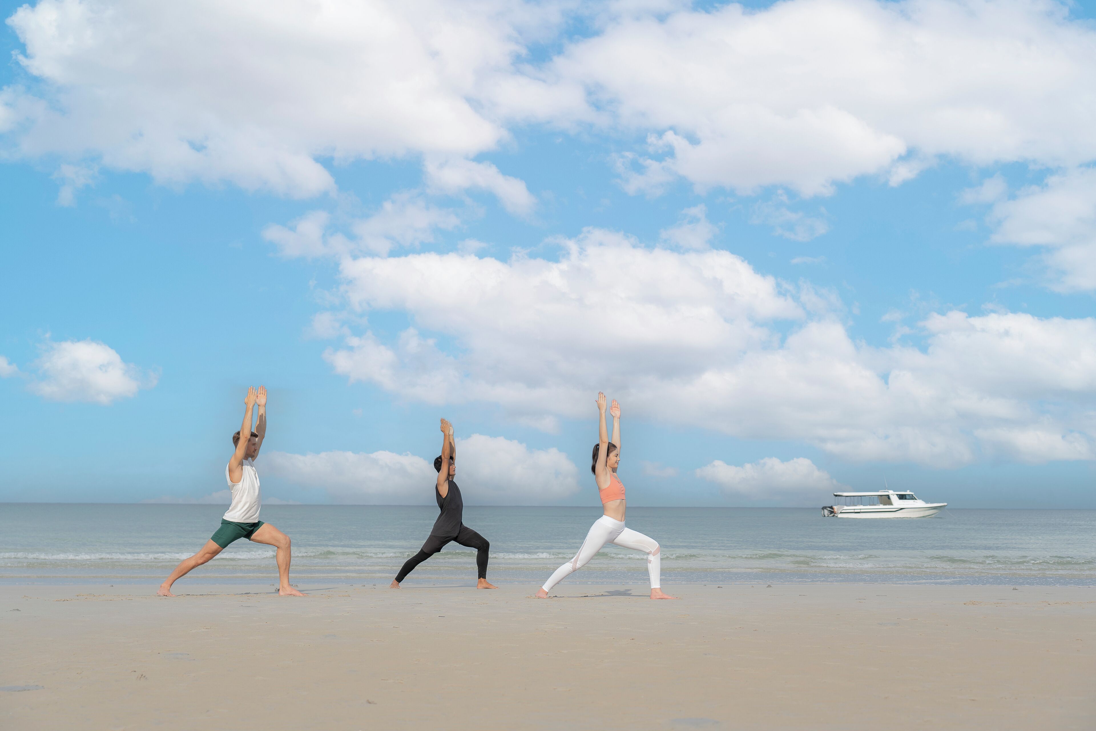 Three people performing yoga on a beach with a boat in the background.