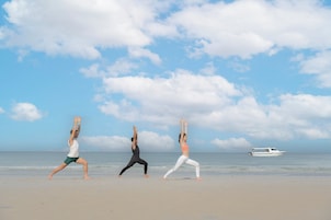 Three people performing yoga on a beach with a boat in the background.