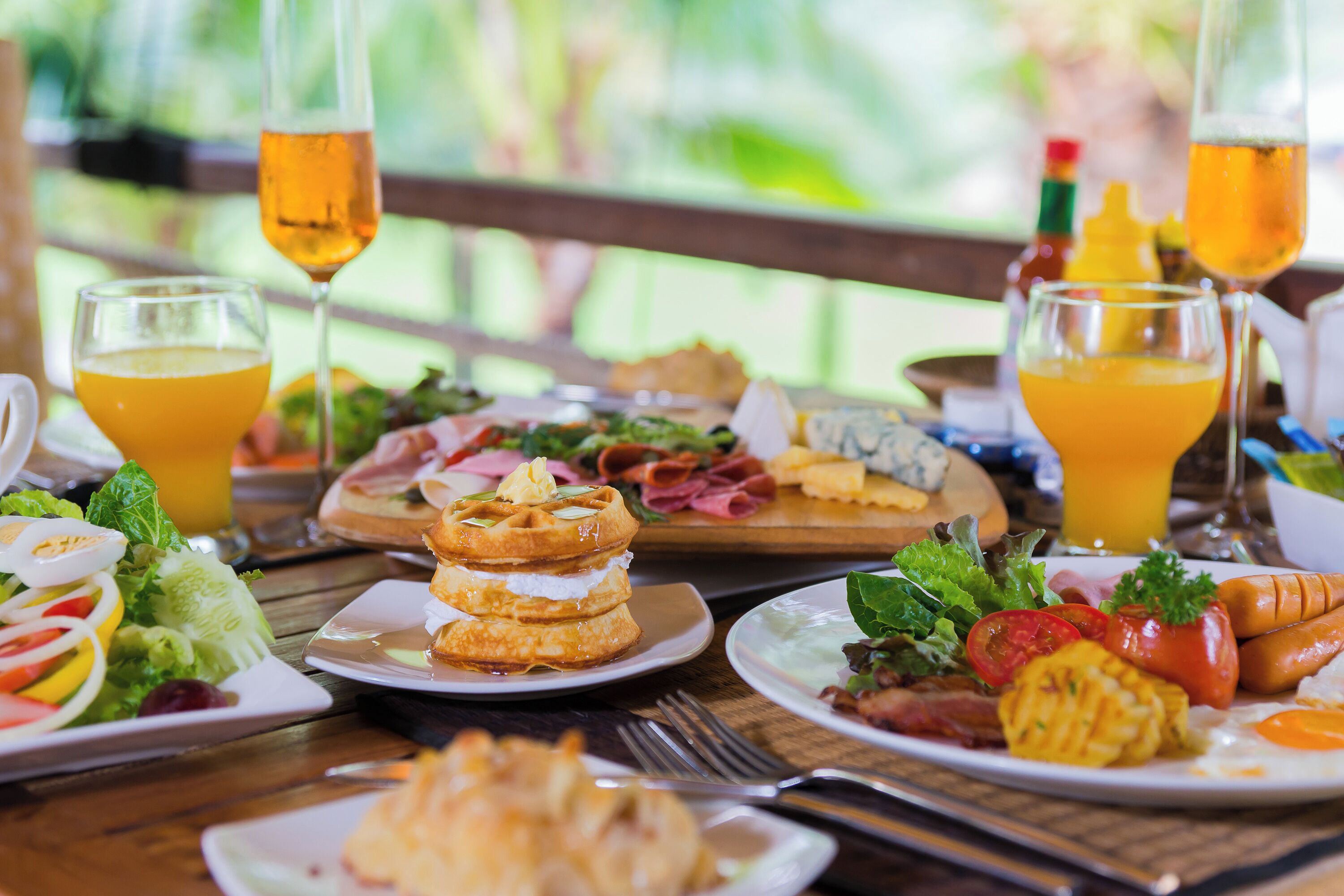 A breakfast buffet with various dishes, drinks, and a wooden table setting.