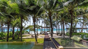 A wooden deck leading to a pool with a netted lounging area, surrounded by palm trees and overlooking the beach. - High Season Pool Villa & Spa (Ko Kood)