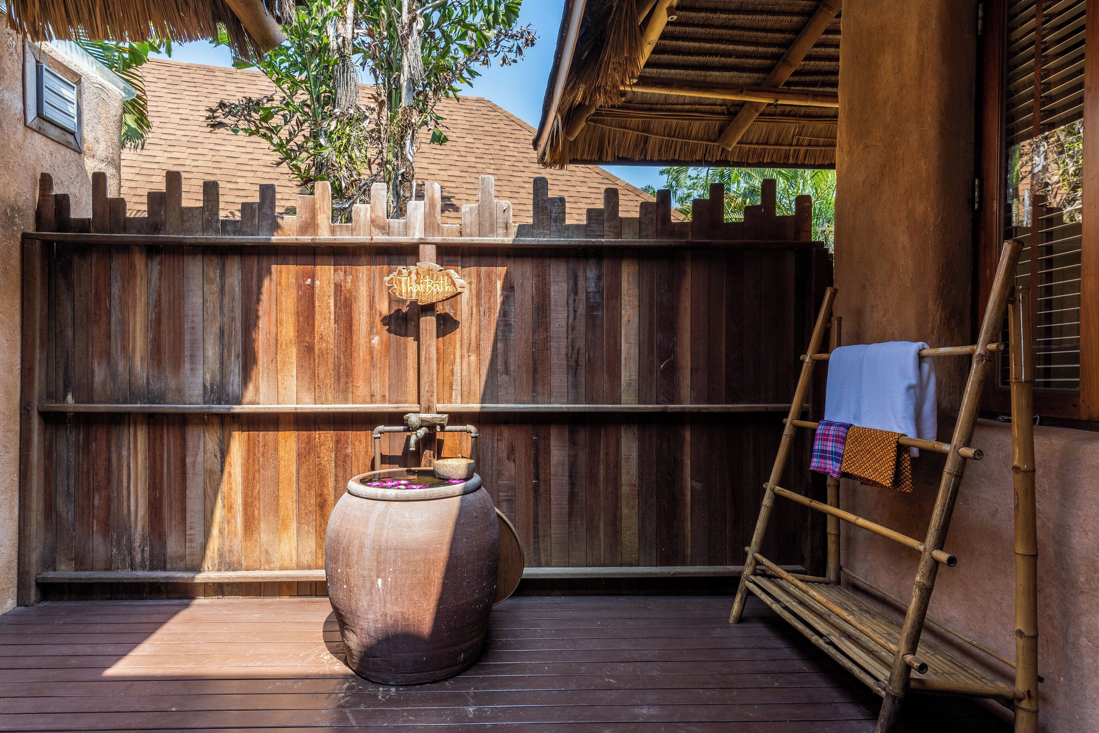 A wooden deck with a large ceramic pot, a wooden ladder, and a thatched roof structure.