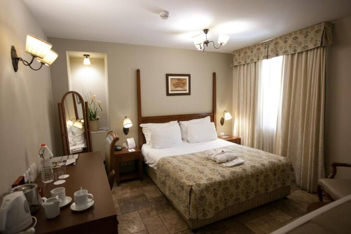 Habitación de hotel con cama, mesitas de noche, escritorio con silla, espejo y ventana con cortinas.