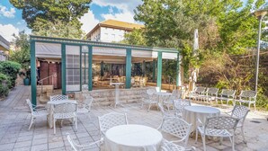 Un patio al aire libre con sillas y mesas de metal blanco, una zona de estar cubierta y un sendero de piedra.