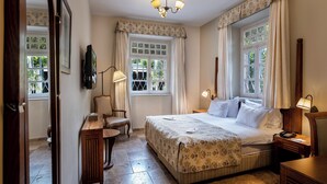 Un dormitorio con una cama grande, dos mesitas de noche, una silla, un escritorio y una ventana con cortinas.