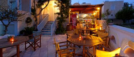 An outdoor patio with wooden tables and chairs, a staircase leading to an upper level, and a Coca-Cola sign.