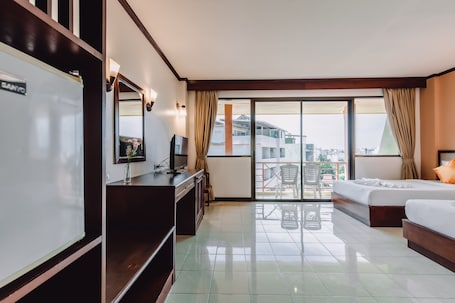 A hotel room with a bed, a desk with a computer, a TV, and a large window with curtains.