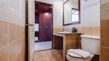Une salle de bain avec des toilettes, un lavabo et un miroir. Une porte donne accès à une autre pièce.