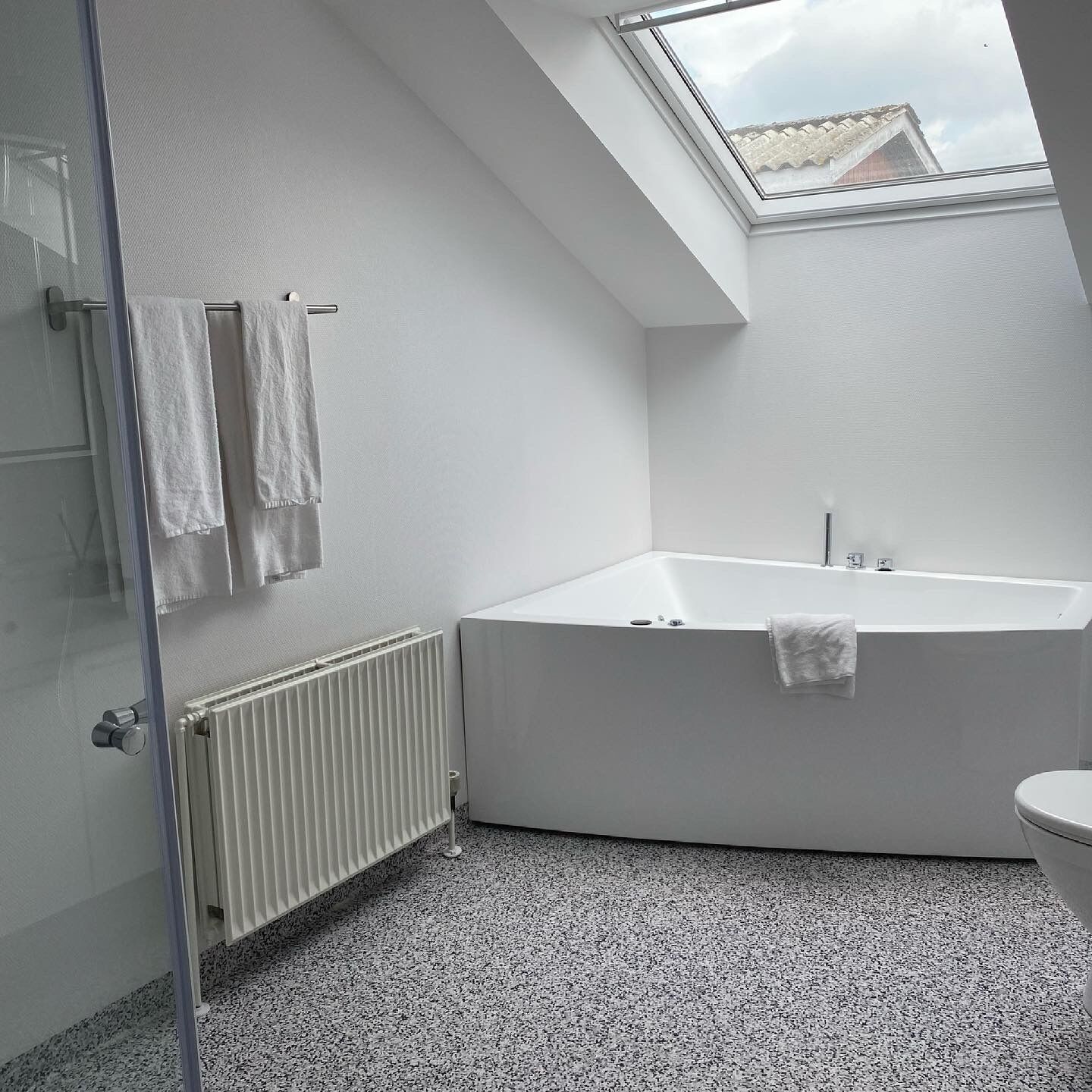 Un baño moderno con tragaluz, una bañera independiente, un inodoro y una cabina de ducha de vidrio.