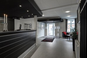 A modern reception area with a black reception desk, a glass door entrance, and a seating area with a red cushion.