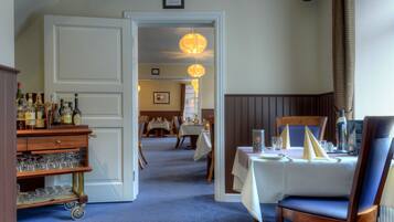 En hotels spiseområde med en barvogn, borde dækket til spisning og en lysekrone.