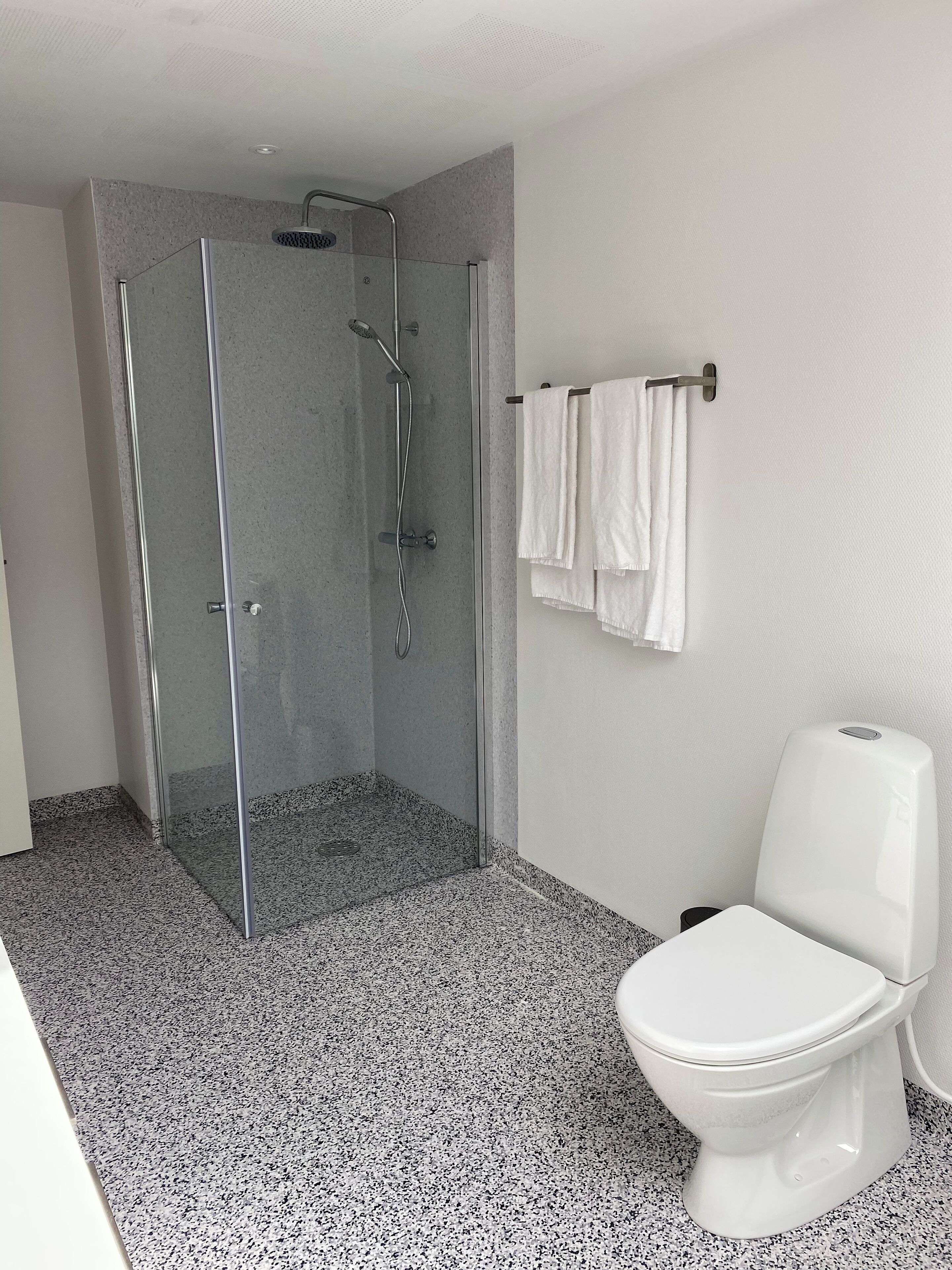 Un baño moderno con ducha de vidrio, inodoro blanco y toallero con toallas blancas.