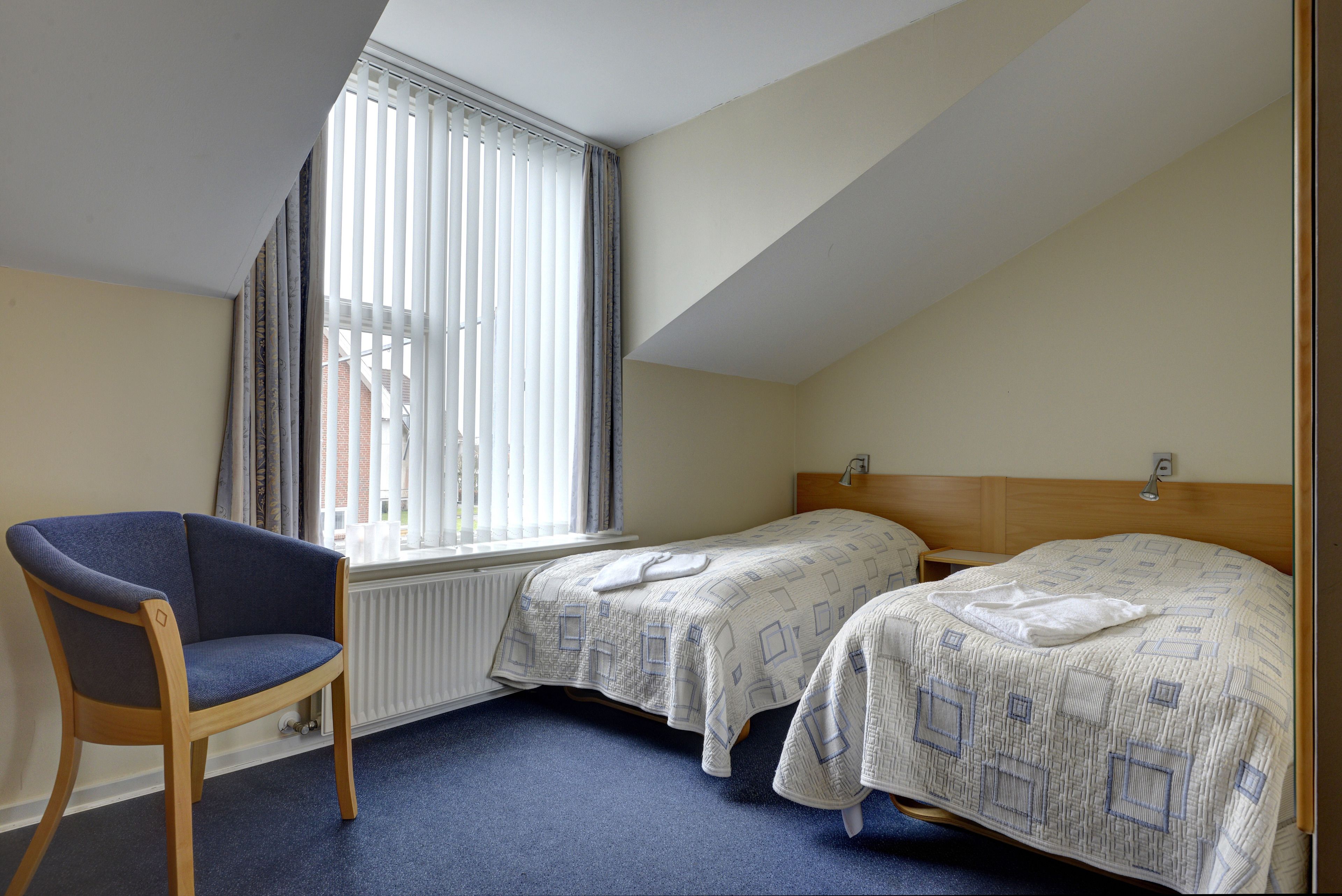 A bedroom with two beds, a chair, and a window with blinds.