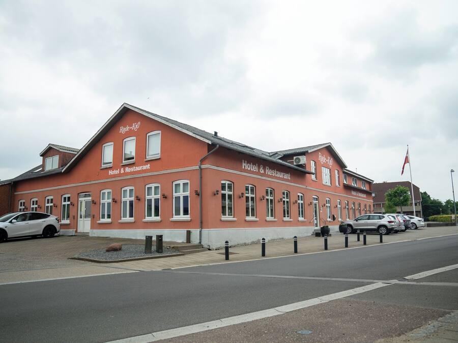 En hotel- og restaurantbygning med en rød facade og hvid dekoration, med flere vinduer og et flag.