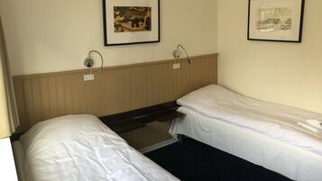 Habitació d'hotel amb dos llits individuals, un capçal de fusta, una làmpada penjada a la paret i dues imatges emmarcades.