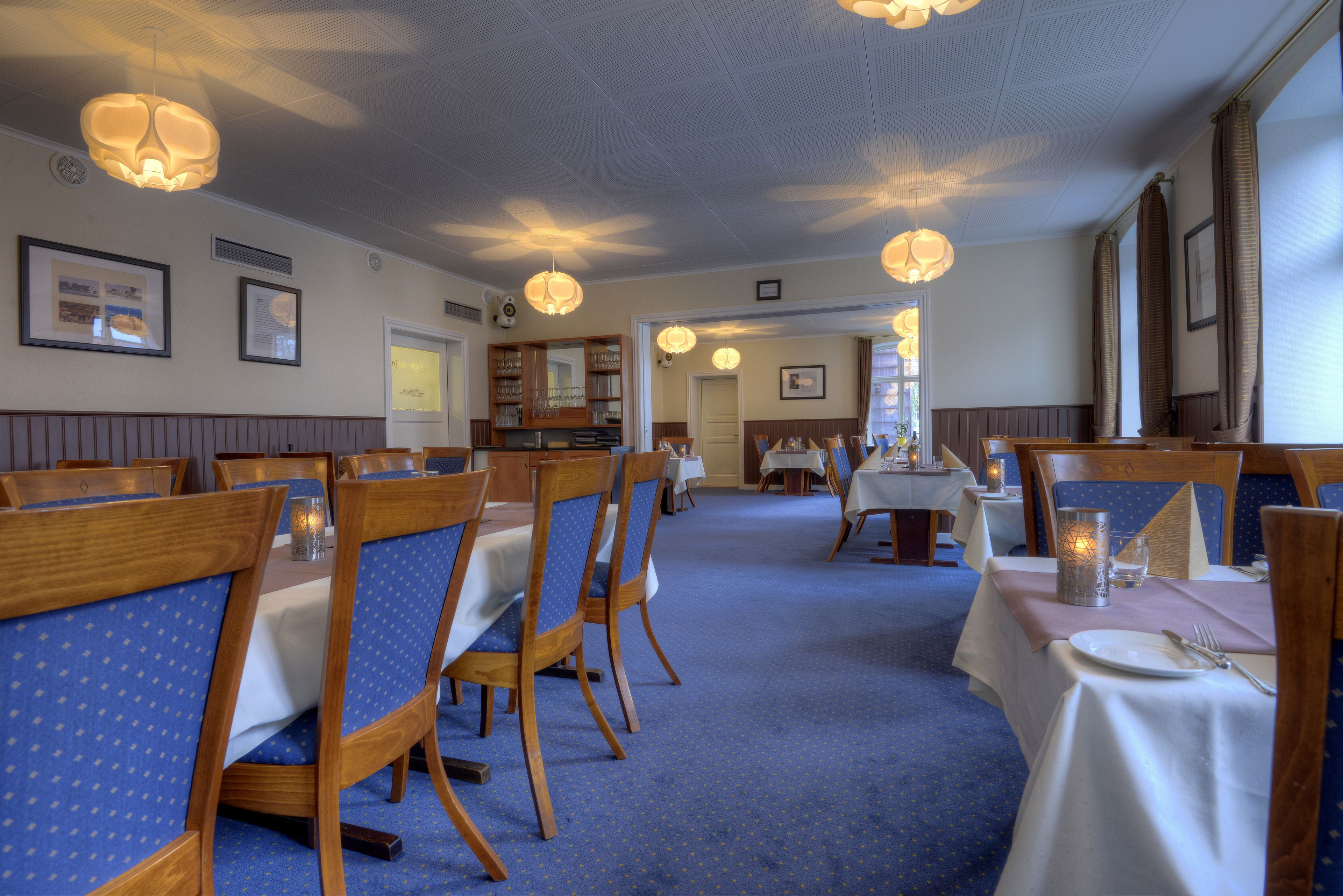 A dining area with wooden tables and chairs, blue upholstered chairs, and pendant lighting.