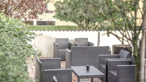 Un patio al aire libre con mobiliario de mimbre, incluyendo sillas y mesas, y una planta en maceta.