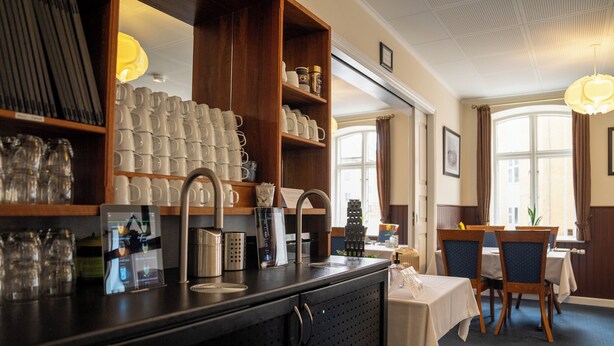 A restaurant with a bar area, shelves with glasses and mugs, and a dining area with tables and chairs.