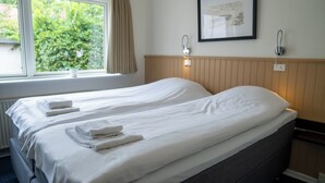 Habitación de hotel con dos camas, ropa de cama blanca, un cuadro en la pared y una ventana con vistas a zonas verdes.