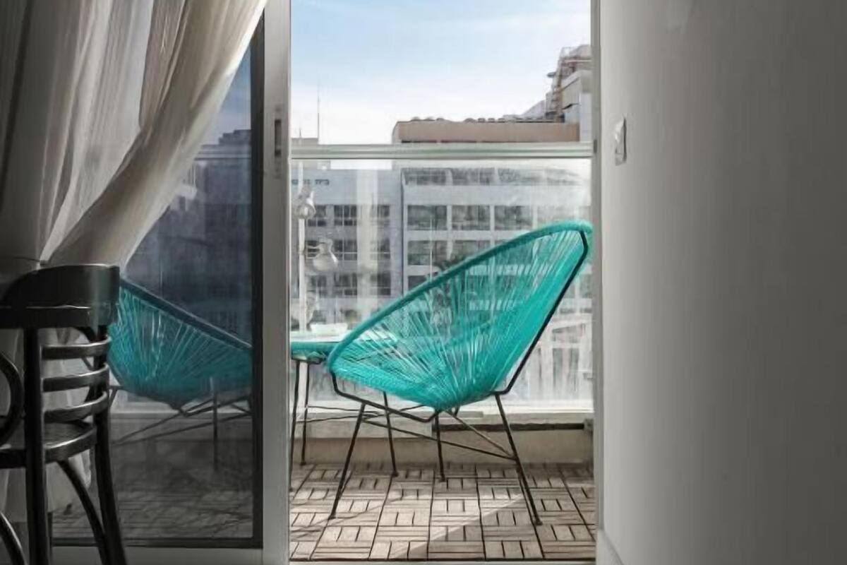 A modern room with a sliding glass door leading to a balcony, a chair, a table, and a wall-mounted lamp.