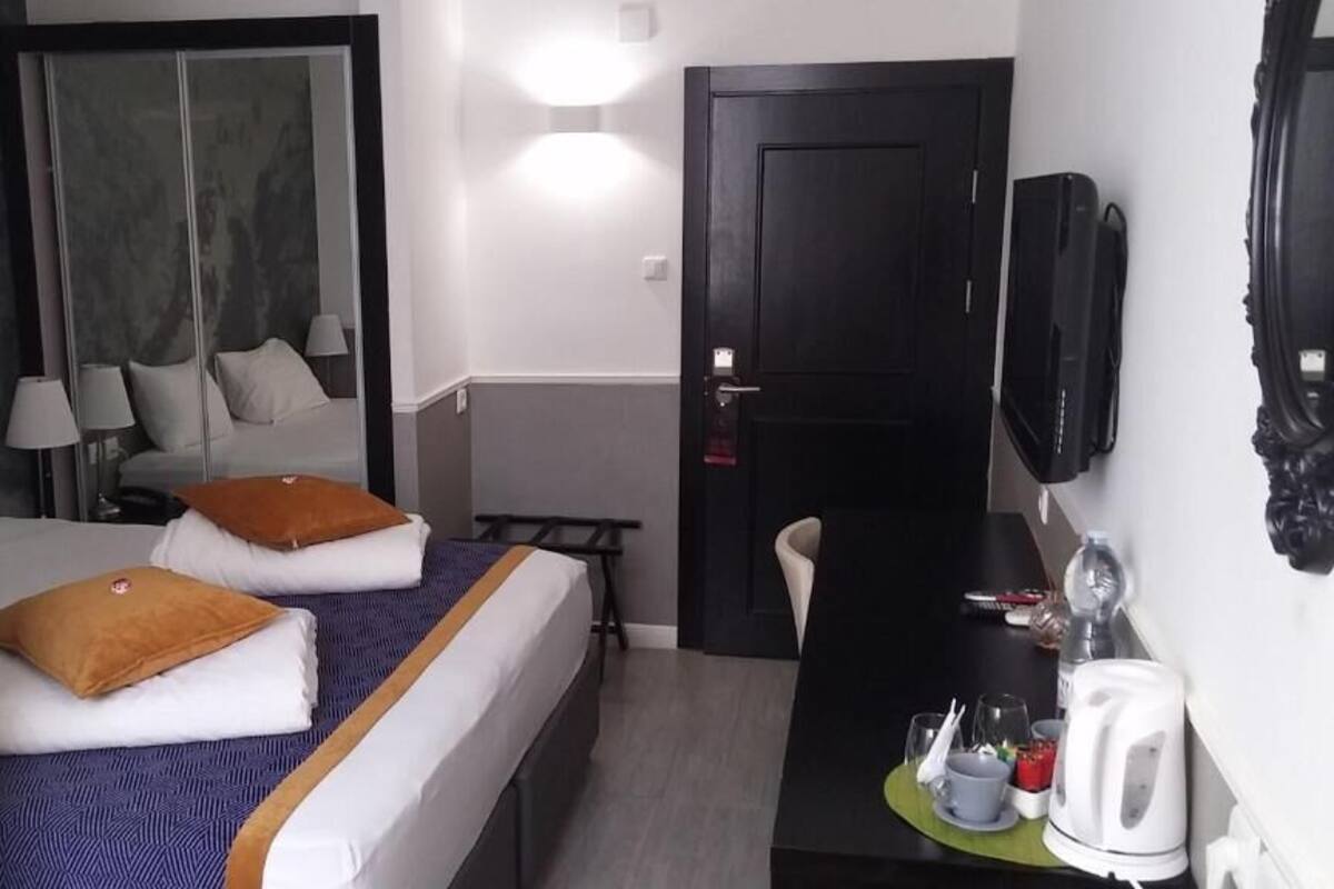 A hotel room with two beds, a desk with a kettle, and a TV.