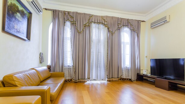 Uma sala de estar com sofá, televisão de tela plana e uma grande janela com cortinas.