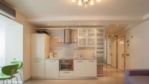 Cozinha moderna com armários brancos, exaustor de aço inoxidável e forno embutido. Há uma cadeira verde e um sofá roxo no ambiente.