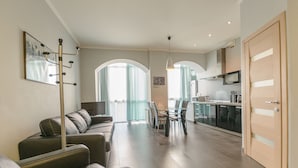 Uma sala de estar moderna com sofá, uma mesa de jantar com cadeiras e uma área de cozinha com micro-ondas e armários.