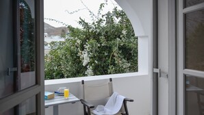 A balcony with a table, chair, and a view of greenery and buildings. - Atlas Boutique Hotel (Santorini)