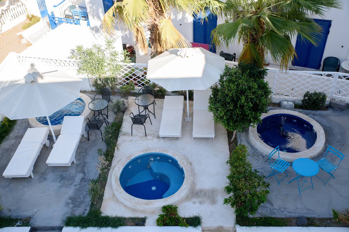 A rooftop pool area with lounge chairs, umbrellas, and a hot tub.