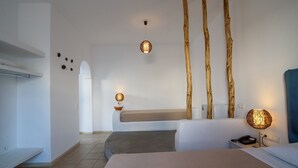 A hotel room with a bed, bedside table, lamp, and a view of a beach through an arched doorway. - Atlas Boutique Hotel (Santorini)