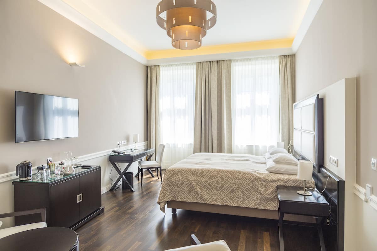 A modern hotel room with a large bed, a desk, a flat-screen TV, and a minibar.