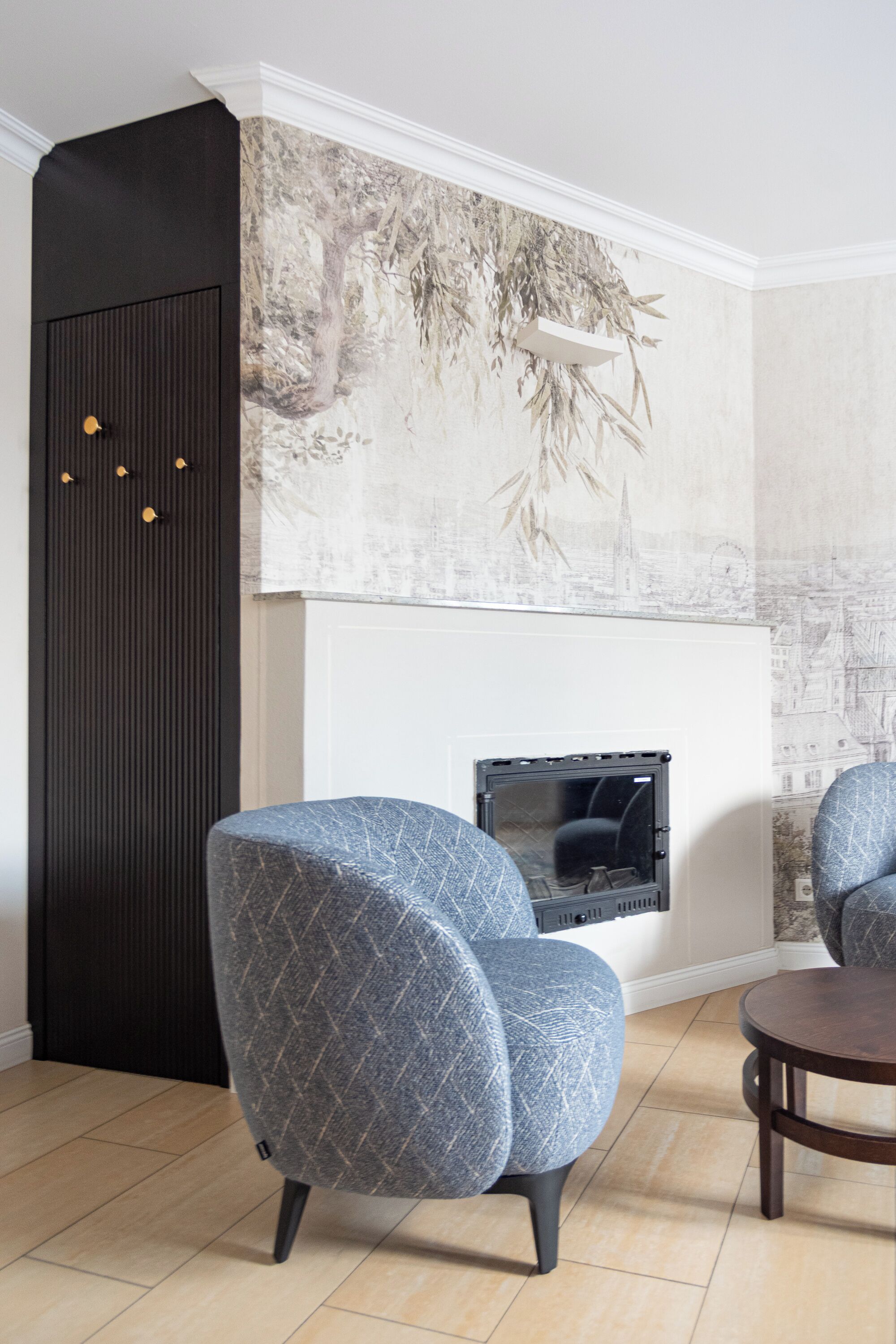 A modern living room with a fireplace, two patterned armchairs, a dark accent wall, and a cityscape mural.
